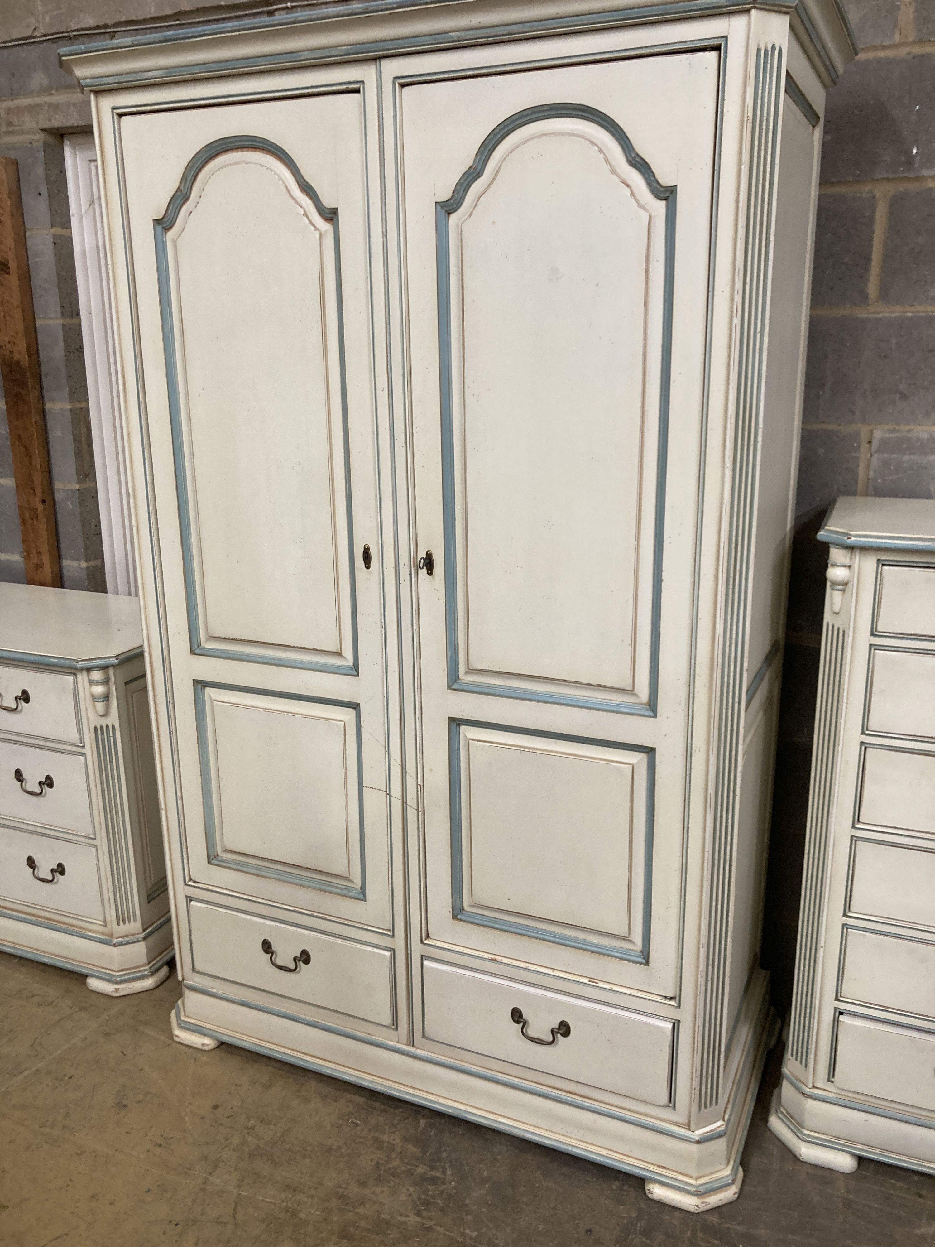 A French provincial style bedroom suite, cream painted, with blue line edging, consisting:- a two door wardrobe, four drawer chest, single bedstead and a tall chest of six drawers, wardrobe W.126cm D.61cm H.202cm